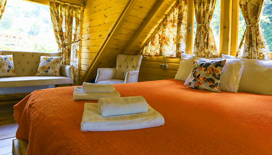 na imagem, vemos um chalé decorado, com lençol na cor laranja, cortinas e estrutura em madeira.