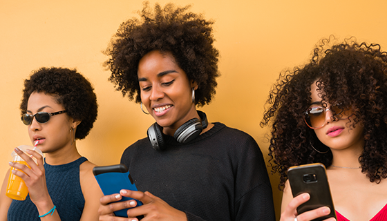na imagem, vemos três mulheres jovens mexendo em seus celulares representando a geração z.