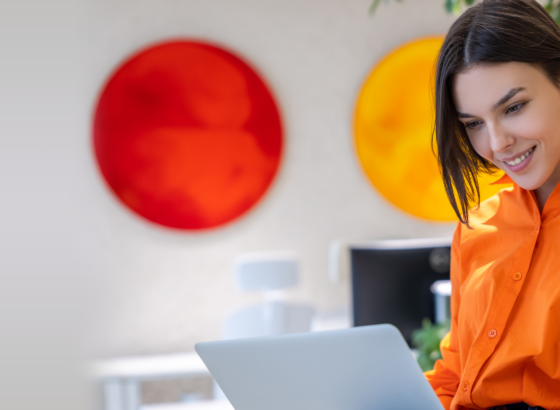 na imagem, vemos uma mulher sorridente em seu notebook. a imagem faz alusão a sua satisfação em estar usando um sistema de reservas online na sua empresa de turismo.