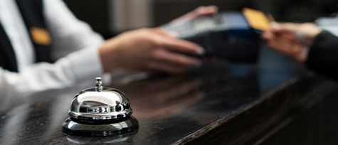 na imagem, vemos uma moça em roupas de concierge, na recepção de uma hospedagem, fazendo o check-in de um turista.