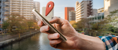 na imagem, vemos uma pessoa segurando um celular. ao fundo, prédios e um lago. a imagem ilustra o conteúdo sobre marketing local.